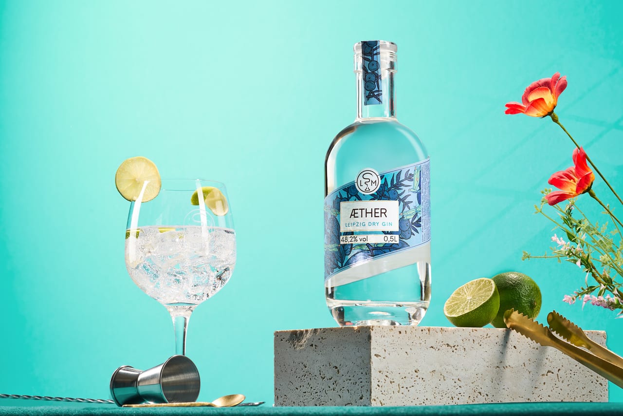 Äther-Gin-Flasche mit Tonic-Glas, Limette und Blüten vor mintgrünem Hintergrund