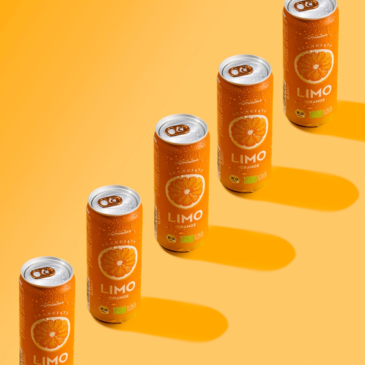 Vier Limo-Dosen Orange diagonal angeordnet mit harten Schatten auf Gelb