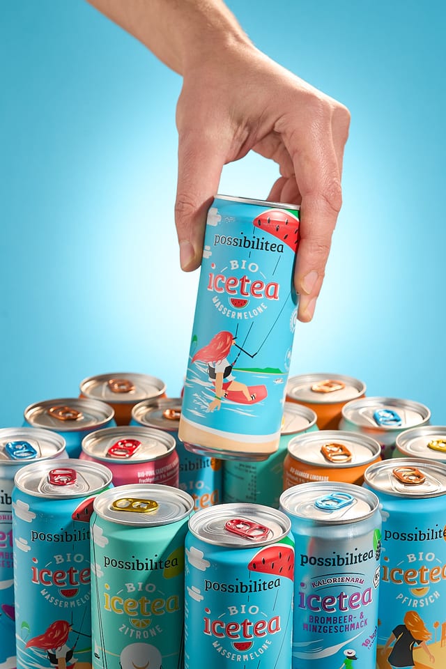 Hand hält eine Eistee-Dose über einer Gruppe weiterer Dosen vor blauem Hintergrund